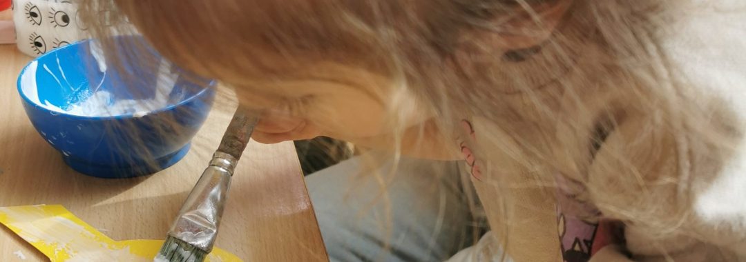 Krippenkind pinselt Leim auf einen Papiervogel