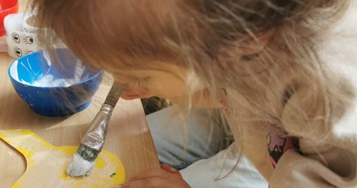 Krippenkind pinselt Leim auf einen Papiervogel