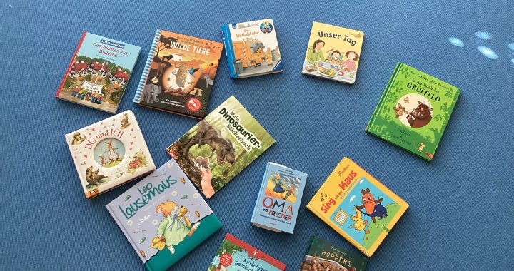 Dreizehn illustrierte deutsche Kinderbücher sind auf einem blauen Teppich in einer lockeren Herzform angeordnet. Die Bücher haben bunte Einbände und zeigen Tiere, Dinosaurier sowie Familienthemen.