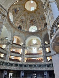 Innenansicht eines großen Kuppelgebäudes mit kunstvollen Fresken, großen Bogenfenstern, komplizierten Balkongeländern und Marmorsäulen, die das natürliche Licht auf die architektonischen Details fallen lassen.