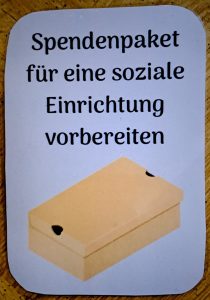 Eine Karte auf einer hölzernen Oberfläche zeigt den deutschen Text Spendenpaket für eine soziale Einrichtung vorbereiten über einer Illustration eines geschlossenen Kartons.