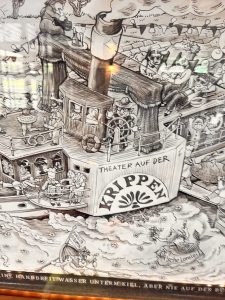 Eine detailreiche Schwarz-Weiß-Karikatur zeigt ein lebhaftes Boot mit der Aufschrift „Theater auf der Krippen“, auf dessen Deck und im Wasser zahlreiche Menschen und Tiere unter einem geschäftigen Himmel ausgelassen feiern.
